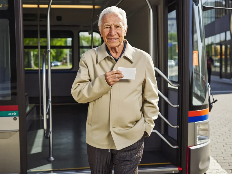 Un uomo anziano sale su un autobus cittadino tenendo in mano una tessera bianca.